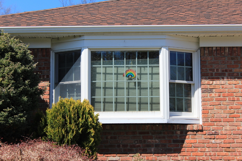 A residential house with a rainbow on a window. 