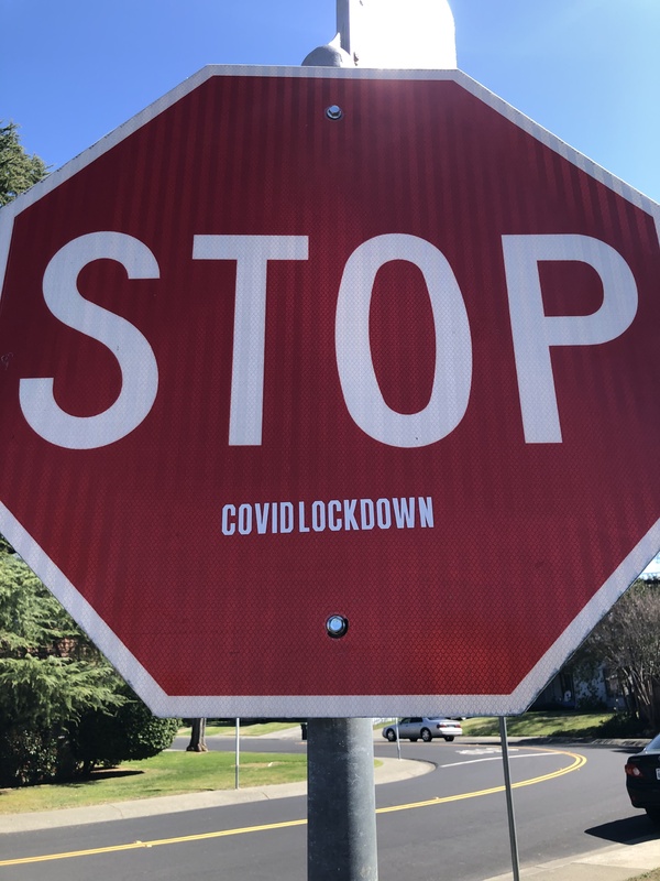 This is a picture of a red stop sign which has a sticker on it reading "STOP... COVIDLOCKDOWN". 