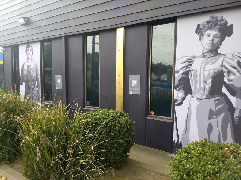 This is a picture taken of two murals that are painted on the side of a building. Two women are depicted in black and white. 