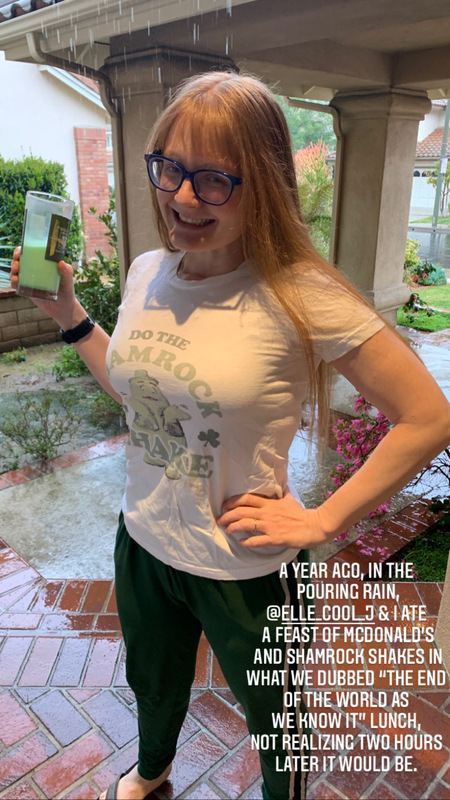 This is a picture taken of a girl smiling and holding a shamrock shake from McDonald's. She is wearing a white shirt, sweatpants, and glasses while rain can be seen falling in the background. A caption at the bottom of the photo reads: "A year ago in the pouring rain, @ellie_cool_j and I ate a feast of McDonald's and shamrock shakes in what we dubbed 'the end of the world as we know it' lunch, not realizing two hours later it would be."