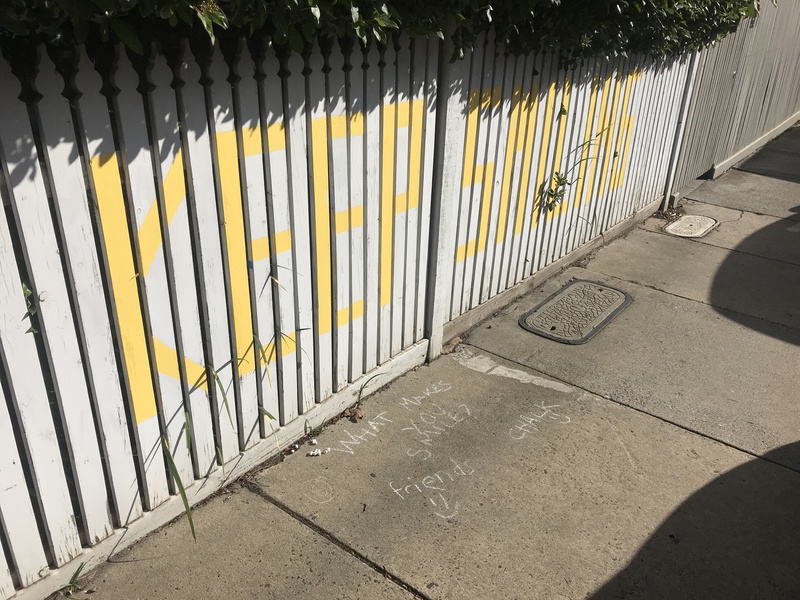 A white fence with writing that says "keep smiling". 