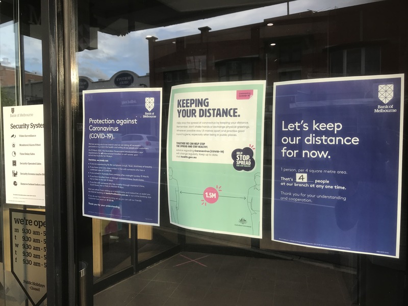 A door that has signs taped on the inside of the glass informing visitors of capacity limits and social distancing. 