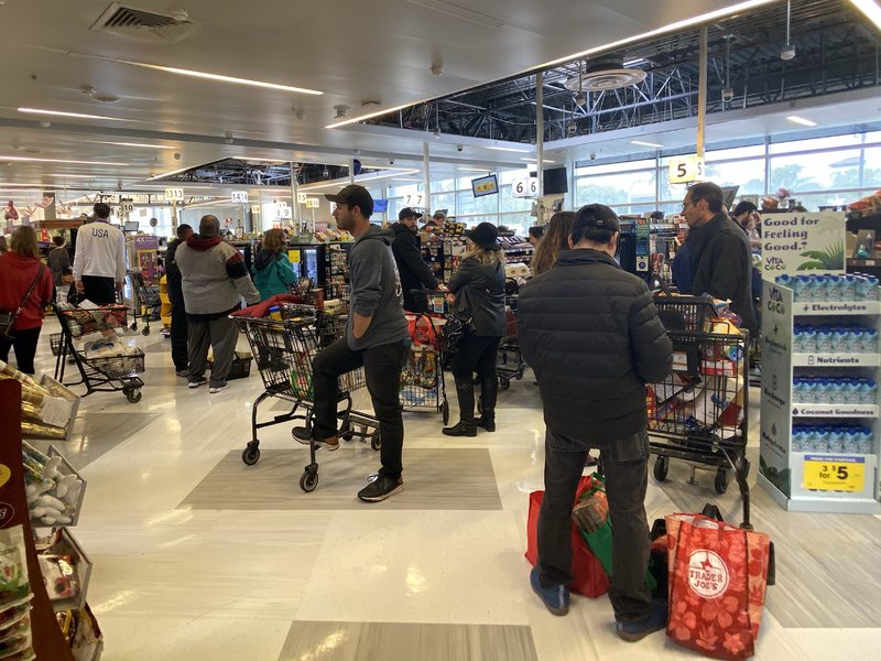 A busy grocery store filled with people standing in lines to check out with grocery carts that are full of food.