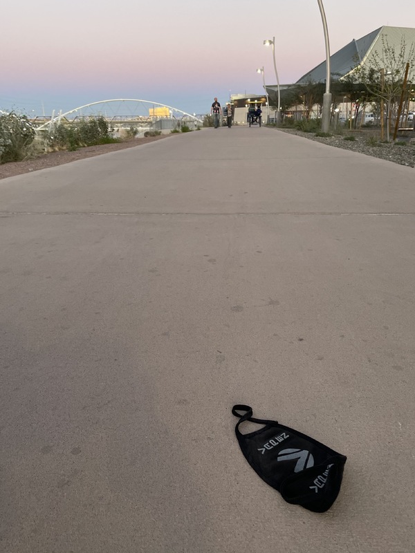 This is a picture of a discarded black cloth face mask left on the sidewalk. 