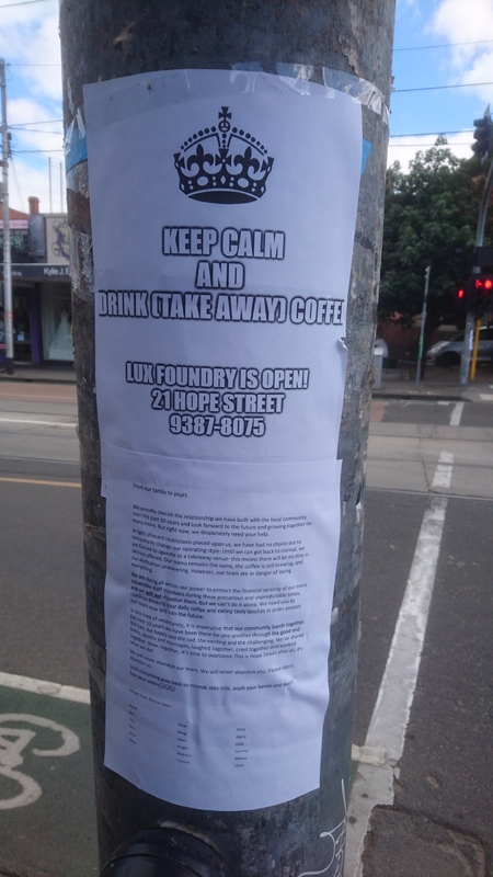 A paper sign that is taped on a light pole. The sign talks about hours of a café that is serving coffee that you can take to go with you. 