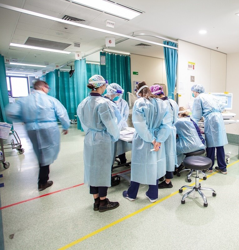 This is a picture of a group of healthcare workers wearing full protective gear gathering around a table in a hospital. 