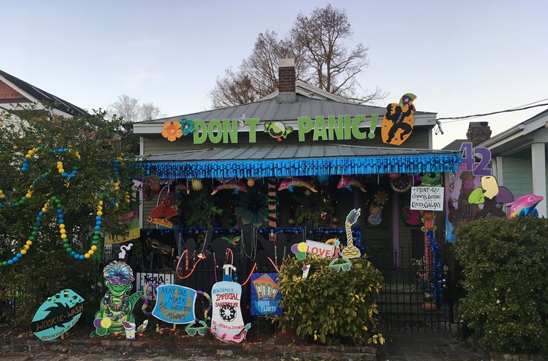 This is a picture taken of a person's house that has been decorated with various COVID-19 related messages or symbols. Some signs depict a container of hand sanitizer or a face mask, while a banner hanging from the roof reads "Don't Panic." 