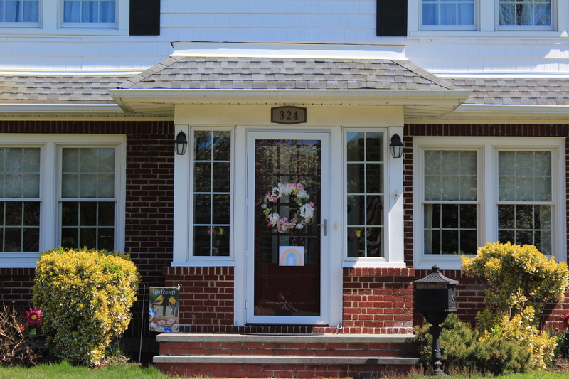 A house has a spring wreath hanging on the front door, along with a drawing of a rainbow.