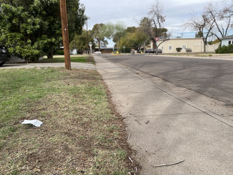 This is a picture of a discarded face mask that has been left on someone's lawn. A residential street can be seen in the background. 