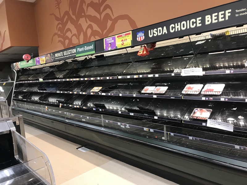 A meat refrigerator section in a grocery store that only has 6 items left. The rest of the shelves are empty. 