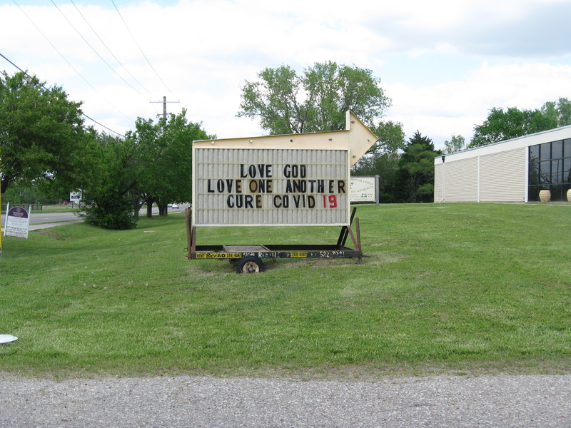 Sign with a big arrow on top with text, "LOVE GOD - LOVE ONE ANOTHER - CURE COVID 19"