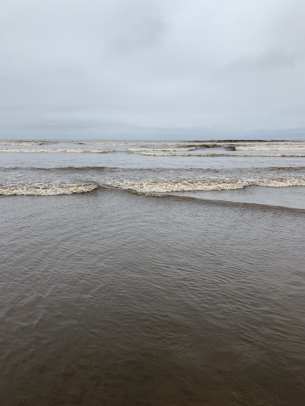 Waves rolling in at the beach under a grey sky. 