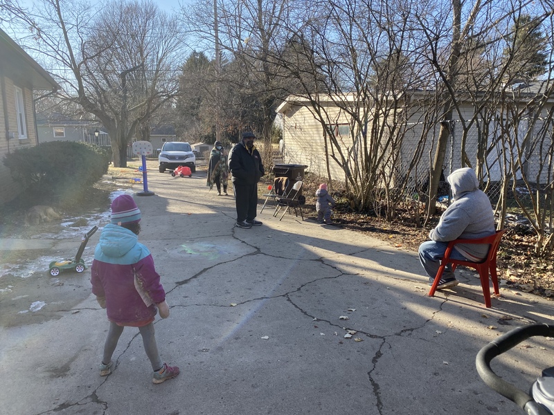 This is a picture of a group of people in winter clothing and face masks doing a socially distanced visit in their driveway. 