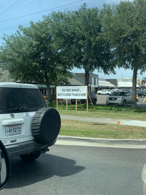 A sign off the side of a road that says "six feet apart...But closer than ever!"