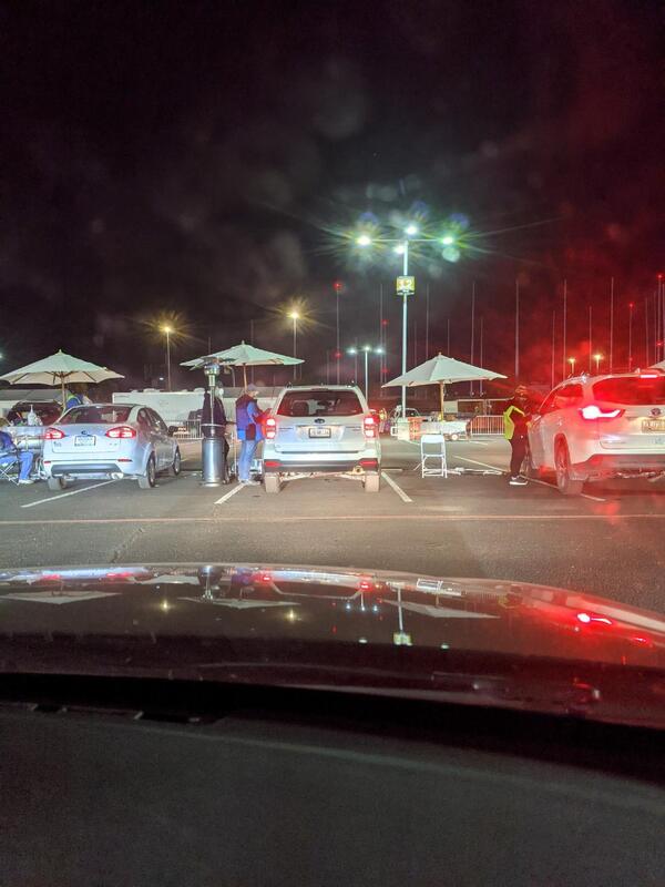 Parked cars with workers at COVID-19 vaccination site.