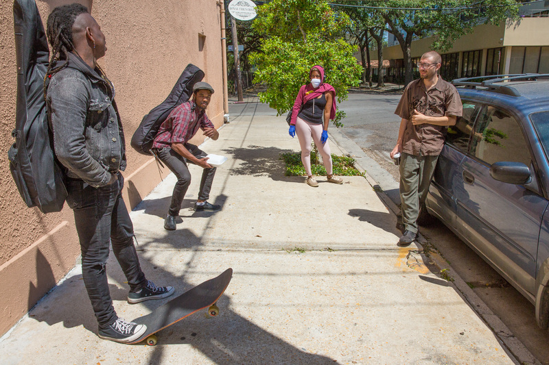 Four people talk on the sidewalk next to a car.