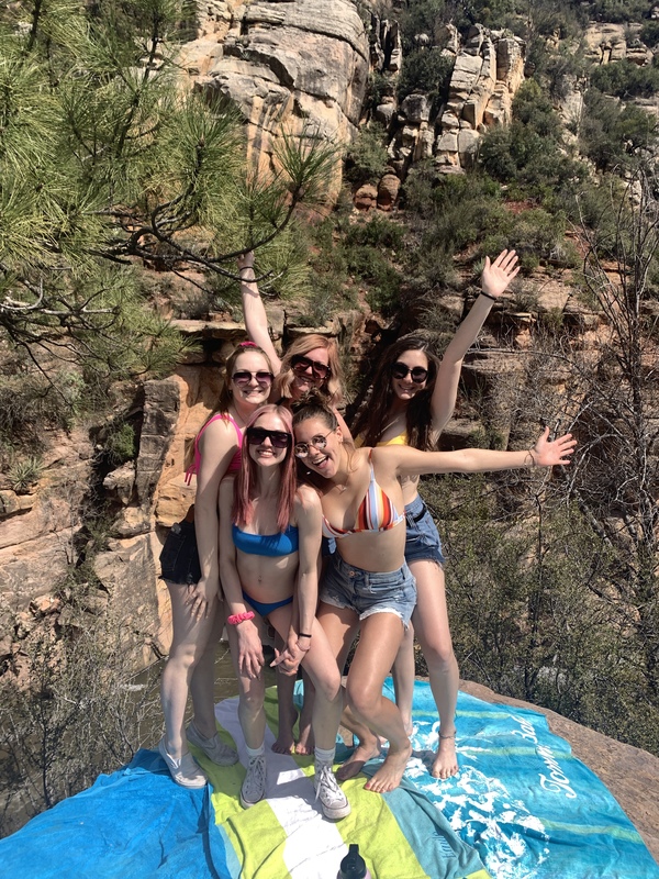 Five people posed on top of a rock standing on top of a deflated tube with a rock formation in the back. 