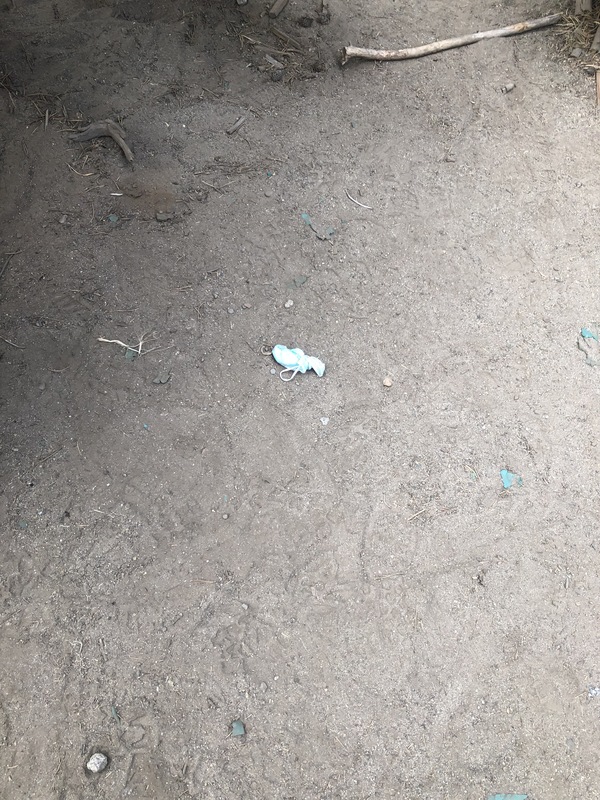 This is a picture of a face mask that has been discarded in the dirt outdoors.  