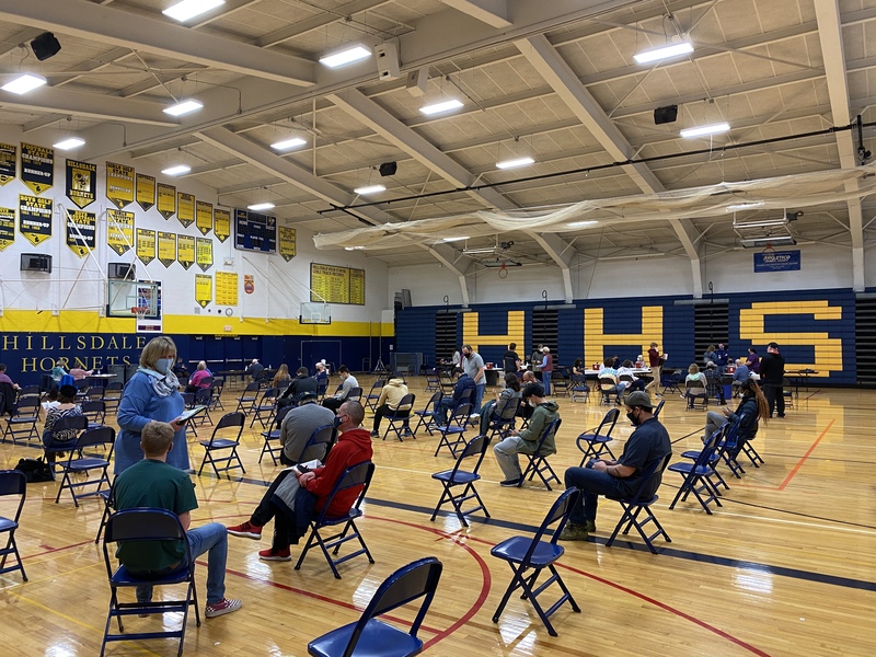 This is a picture of a vaccination center that has been set up inside what appears to be an high school gymnasium. 