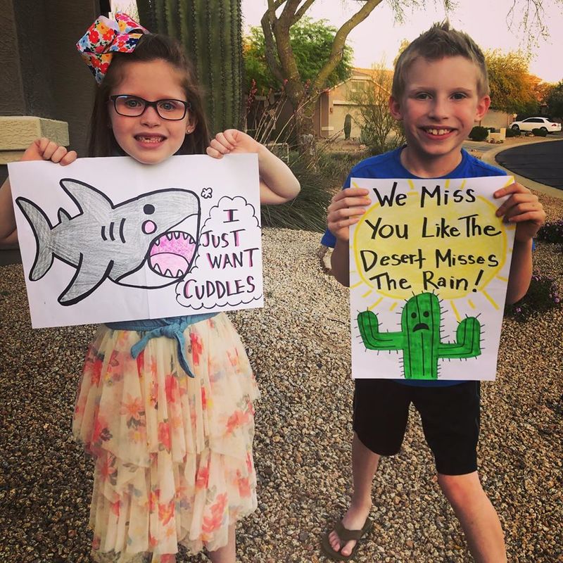 Two children holding up drawings outside. 