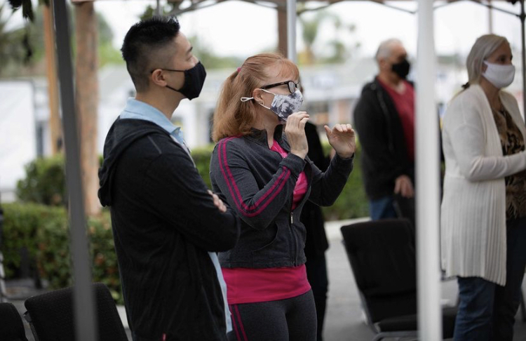 This is a picture taken of a group of people standing outside while wearing face masks. 