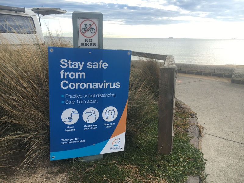 A sign that is before a sidewalk to the beach that talks about practicing social distancing, to cough into your elbow, and to wash your hands. 