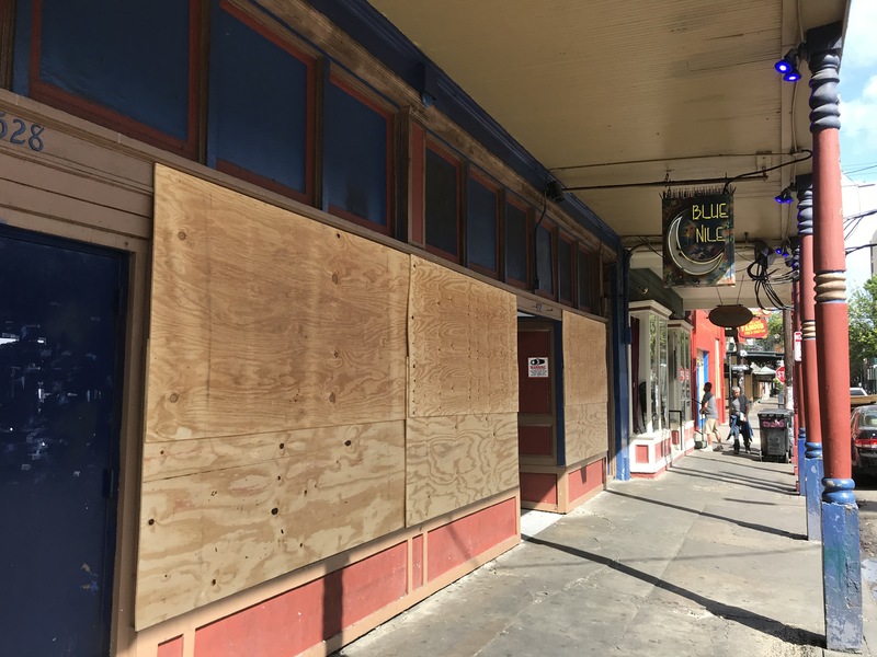 A store with wood over the windows. Hanging from the awning is a sign with a moon on it that says: Blue Nile. 