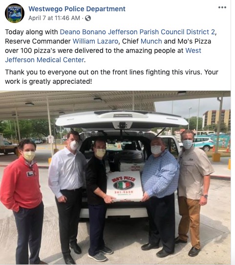 Five men holding a pizza with multiple pizzas in a car behind them. 