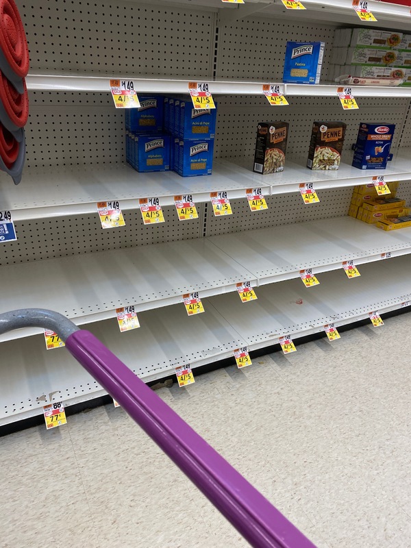 A pasta aisle at a grocery store. The shelves only have a handful of pasta boxes left. 