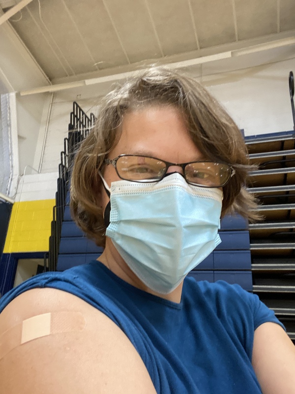 This is a picture of a women who is wearing a mask and glasses posing for a photo after receiving a vaccination shot.  