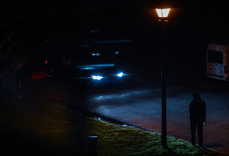 A hooded person standing in front of a car. 