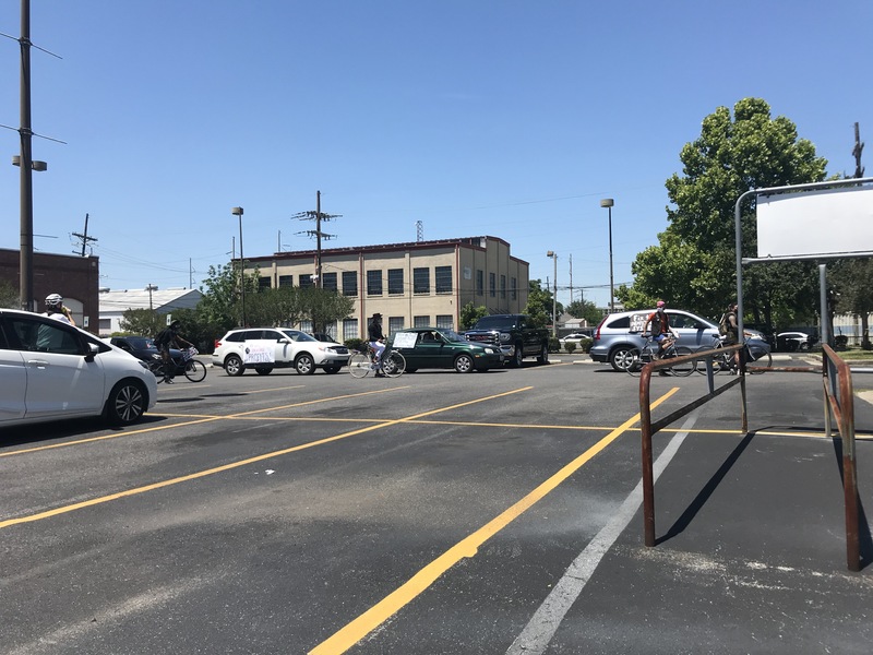 Blue sliver SUV, green car, white SUV, black SUV, and five cyclists are in the protest line. All four vehicles have signs hanging off the passenger side. 