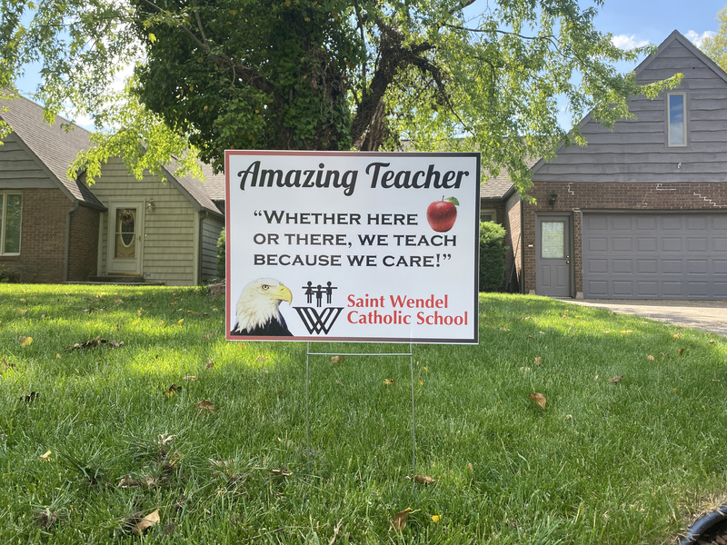 A yard sign reading "Amazing Teacher: Whether Here or There, We Teach Because We Care".