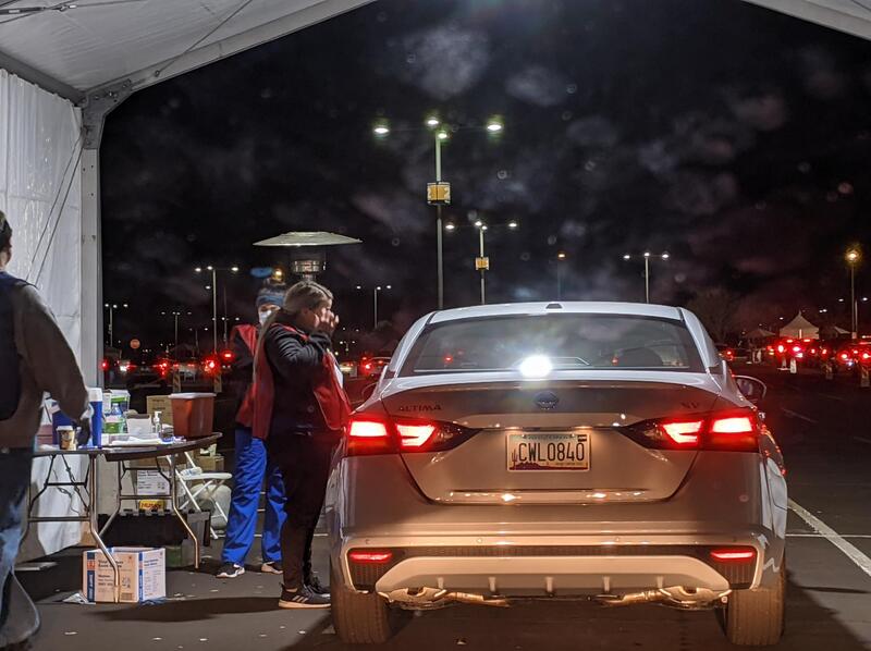 Worker standing next to car at night during COVID-19 drive-thru vaccination.