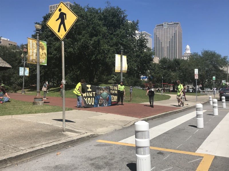 Protestors outside an entrance to Duncan Plaza in New Orleans, Louisiana holding a banner with Uncle Sam in a face mask with text saying, "I want you to die for the economy." 