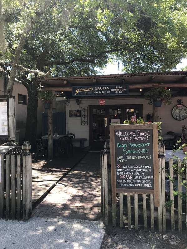 This is a picture taken of the outside seating area of a restaurant which has recently reopened. A sign welcomes patrons, but also reminds them to remain socially distant. 