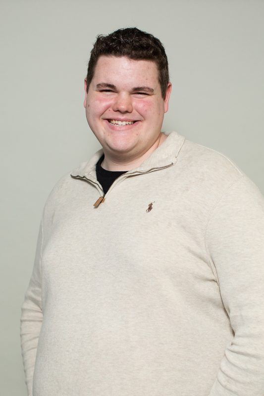 A young person smiling with curly brown hair and a white sweater. 