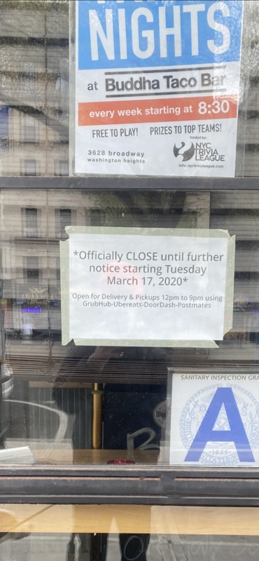 Window for Buddha Taco Bar with 2 signs. Top sign with text, "...NIGHTS at Buddha Taco Bar: every week starting at 8:30: NYC Trivia League" and bottom sign with text, "*Officially CLOSE until further notice starting Tuesday March 17, 2020*: Open for Delivery & Pickups 12pm to 9pm using GrubHub-Ubereats-DoorDash-Postmates"