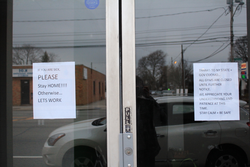 Two signs on entrance of a gym. 
First sign says: "If you are sick, please stay home! Otherwise... Lets work."
Second sign says: "Thanks to NY state and Gov Cuomo all gyms are closed until further notice. We appreciate your understanding and patience at this time. Stay calm and be safe."  