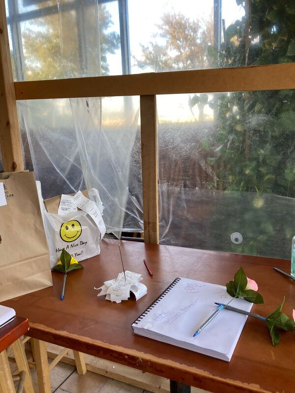 This is a picture of a wooden desk were pens, receipts, and a notebook are set. Two bags sit nearby that appear to be food orders that have yet to be picked up 