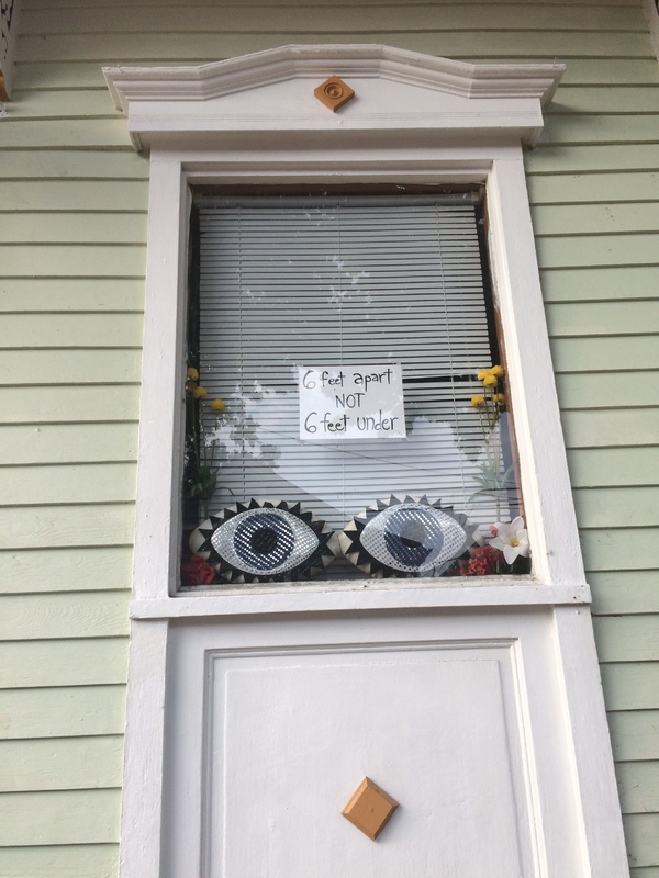 A residential window with a sign that says "6 feet apart nor 6 feet under."