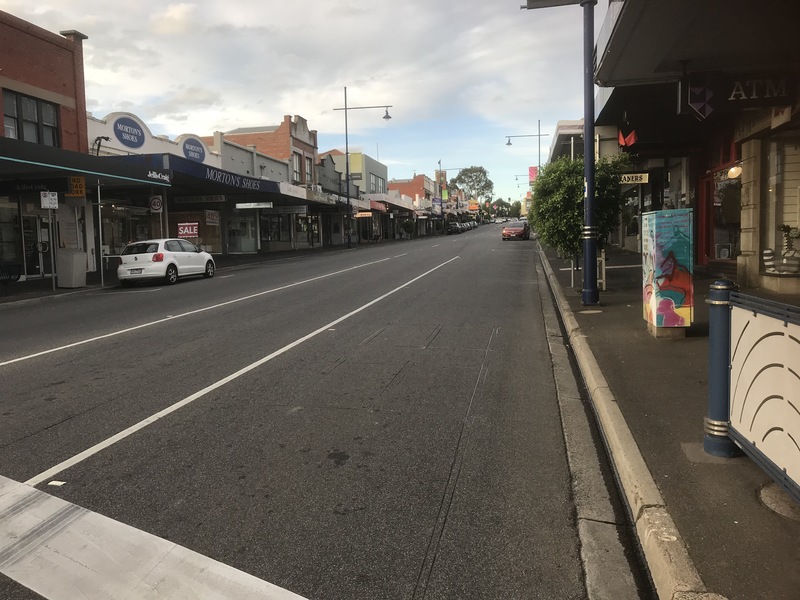 A street with two cars parked off to the side. The road is covered on both sides of it with businesses. 