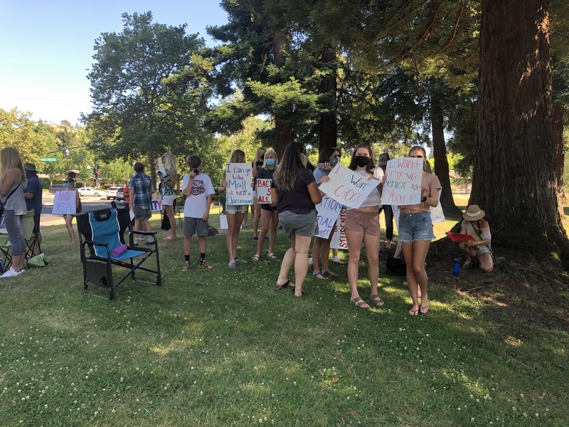 This is a picture taken of a group of people holding signs and protesting. Many are wearing face masks. 