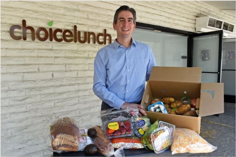 A man posing with a box of food displayed on a table.