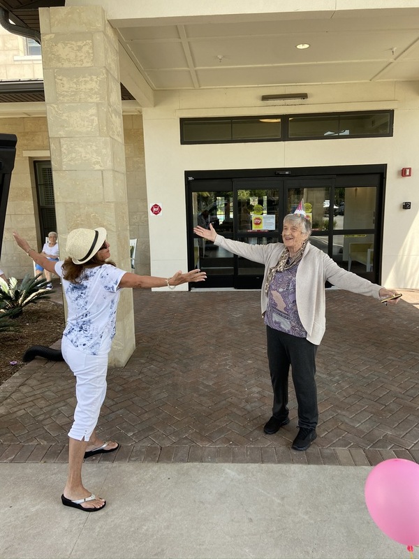 This is a picture taken of two older women having a socially distanced hug, while wearing birthday hats. 