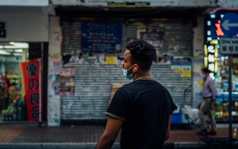 A person with a mask standing on the sidewalk. 