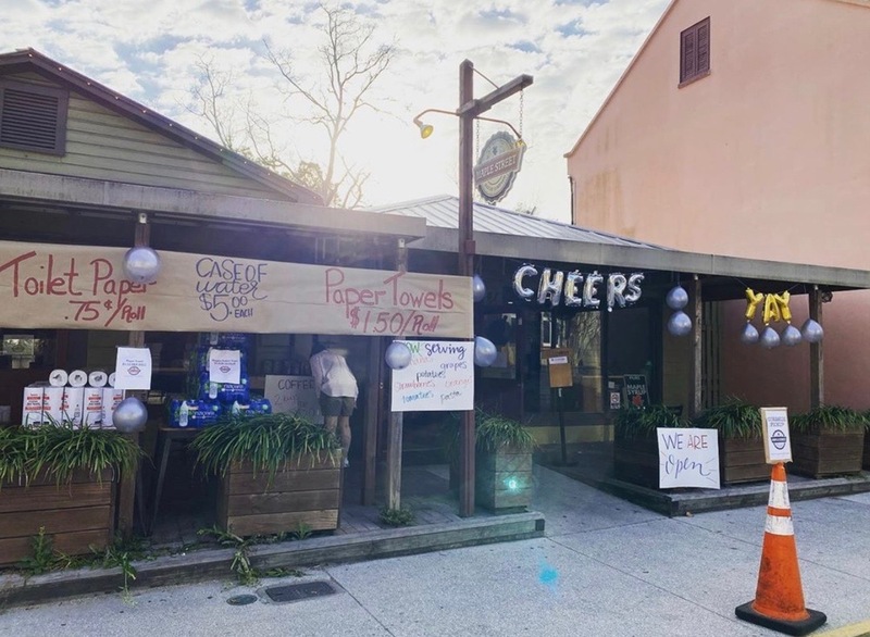 This is a picture taken of a store front, which has several signs advertising the sale of paper products and water. 