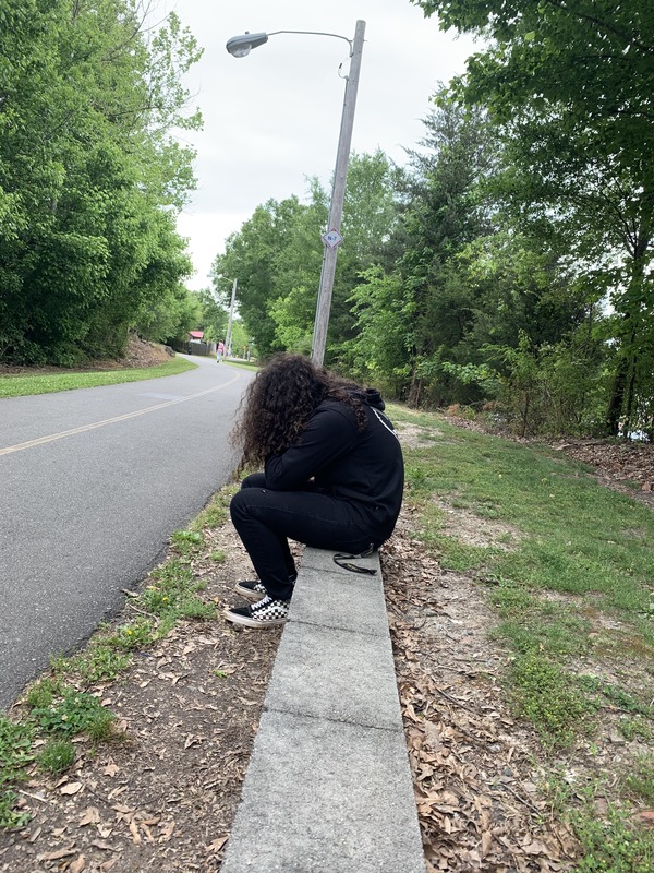 A girl sitting on a sidewalk about 6 feet away from the person who took the photo 