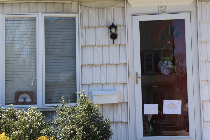 Residential house with a rainbow drawing in the front left window and two rainbow drawings on the front screen door. 