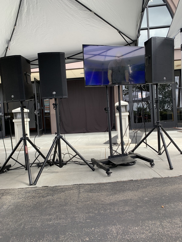 This is a picture taken of several speakers and a television sitting under an overhang outside. 